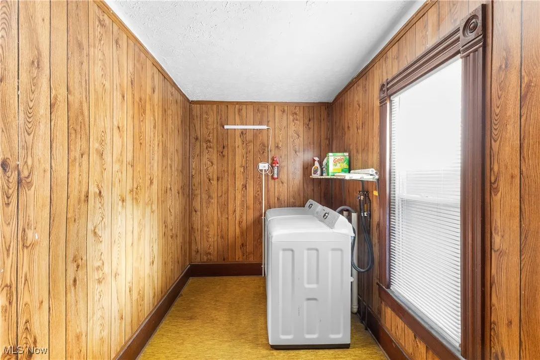 Laundry area with wood walls, washer and dryer, and a textured ceiling