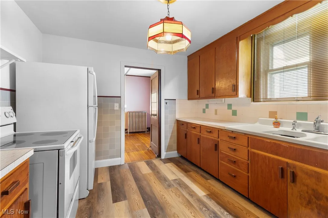 Kitchen featuring white electric range, brown cabinetry, light wood-type flooring, light countertops, and wainscoting