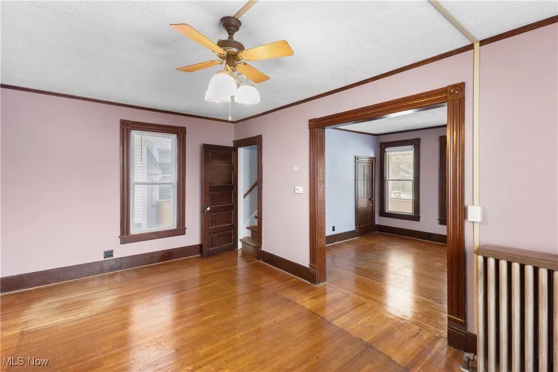Empty room with wood finished floors, ornamental molding, a textured ceiling, ceiling fan, and stairs
