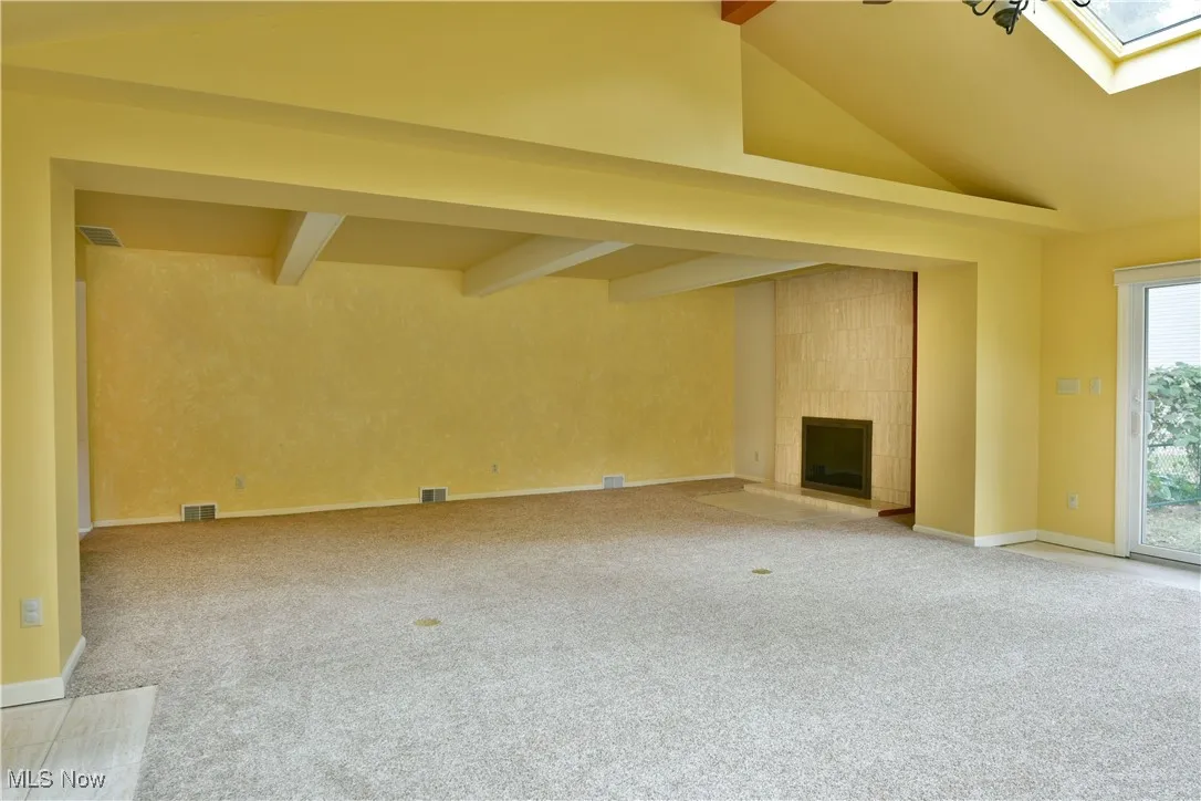 Unfurnished living room featuring a skylight, light colored carpet, and a tiled fireplace