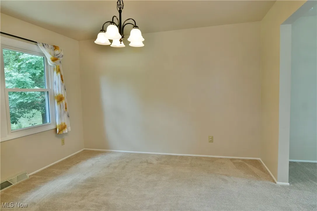 Carpeted empty room with baseboards and a chandelier