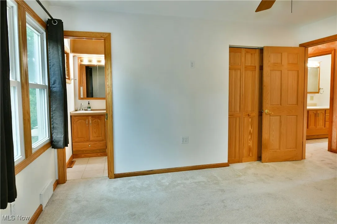 Unfurnished bedroom with ensuite bath, a closet, light carpet, and a ceiling fan