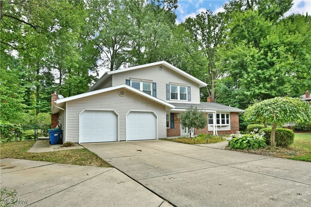 Traditional-style house with driveway, view of wooded area, a garage, a chimney, and brick siding
