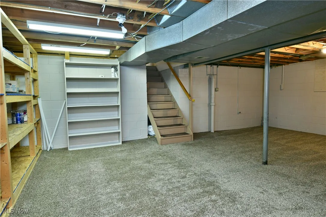 Unfinished basement with stairway and light colored carpet