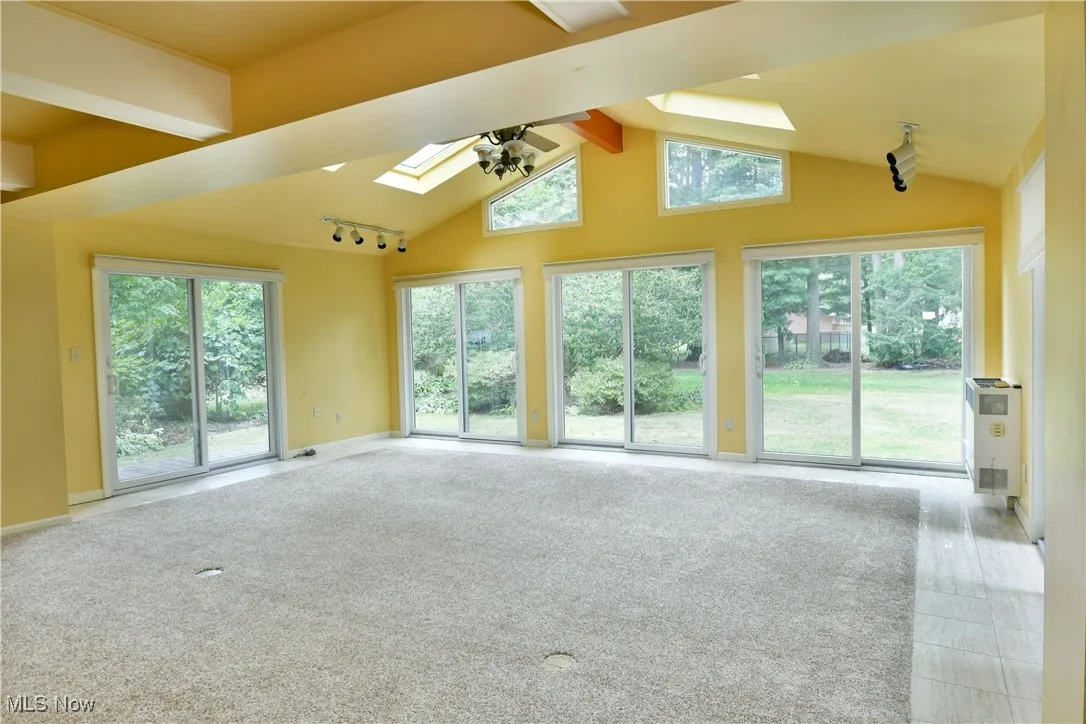 Unfurnished living room featuring high vaulted ceiling, beamed ceiling, ceiling fan, a skylight, and rail lighting