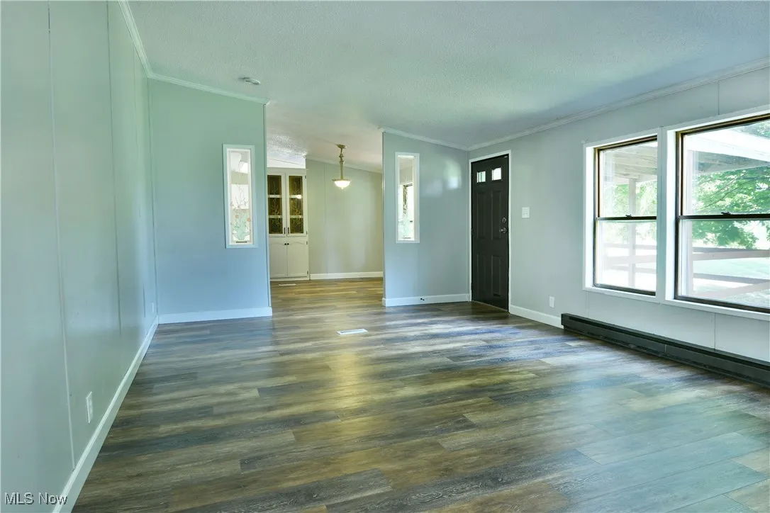 Unfurnished living room with ornamental molding and dark wood-type flooring