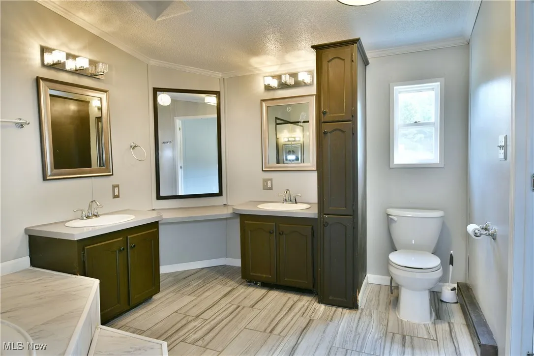 Full bath with a textured ceiling, two vanities, crown molding, and wood tiled floors