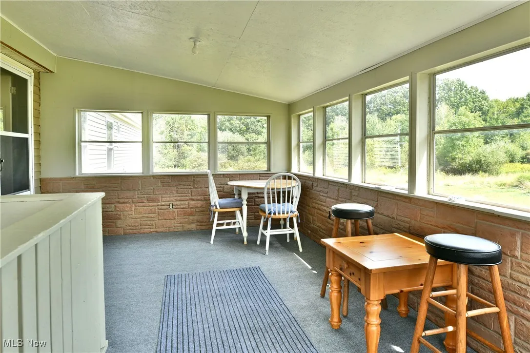 Sunroom / solarium featuring brick wall, vaulted ceiling, carpet, and a textured ceiling