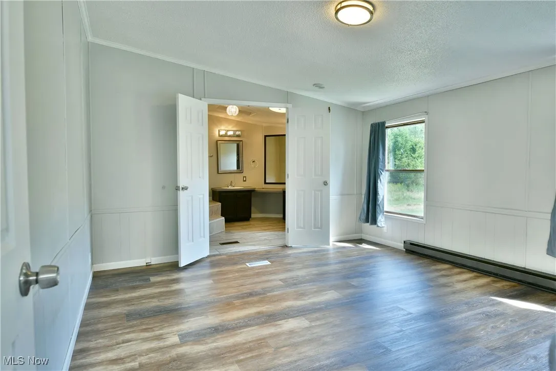 Unfurnished room featuring wood finished floors, vaulted ceiling, crown molding, wainscoting, and a decorative wall