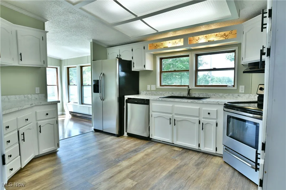 Kitchen featuring stainless steel appliances, light countertops, a textured ceiling, ornamental molding, and light wood finished floors