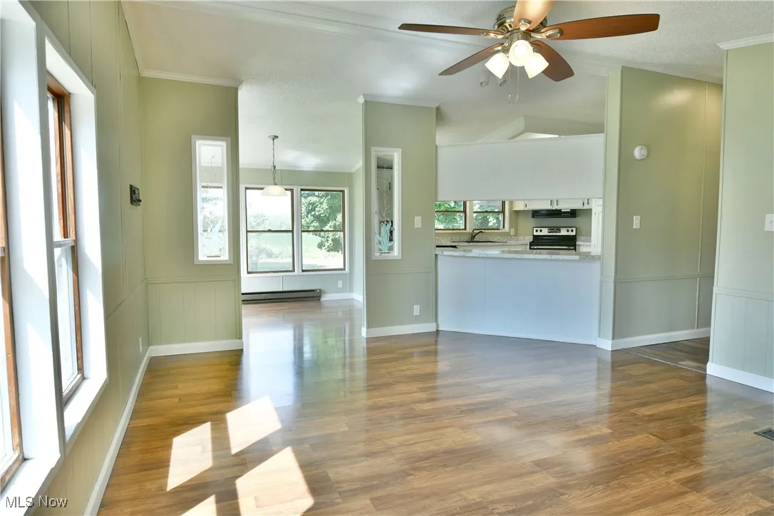 Unfurnished living room with crown molding, wainscoting, wood finished floors, a decorative wall, and a ceiling fan