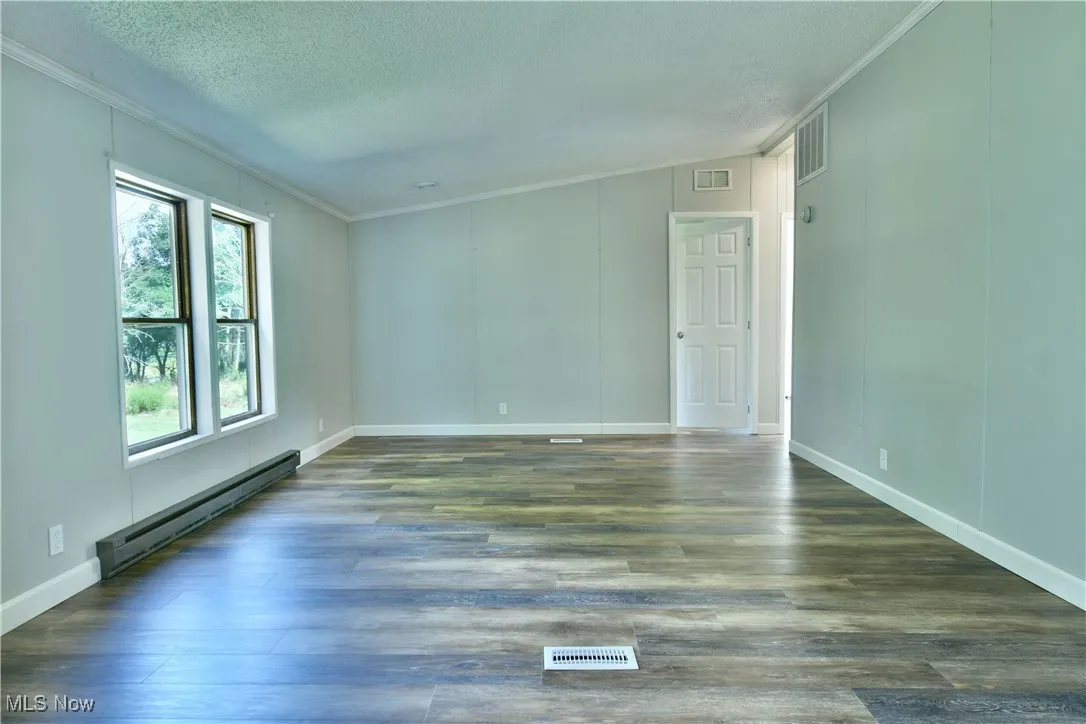 Empty room with crown molding, baseboard heating, dark wood-style floors, a textured ceiling, and a decorative wall