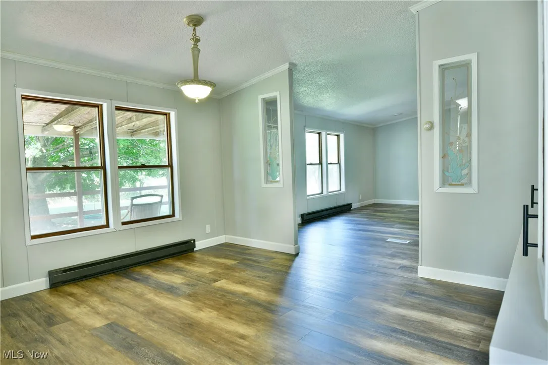 Empty room featuring a textured ceiling, ornamental molding, baseboard heating, and dark wood-type flooring