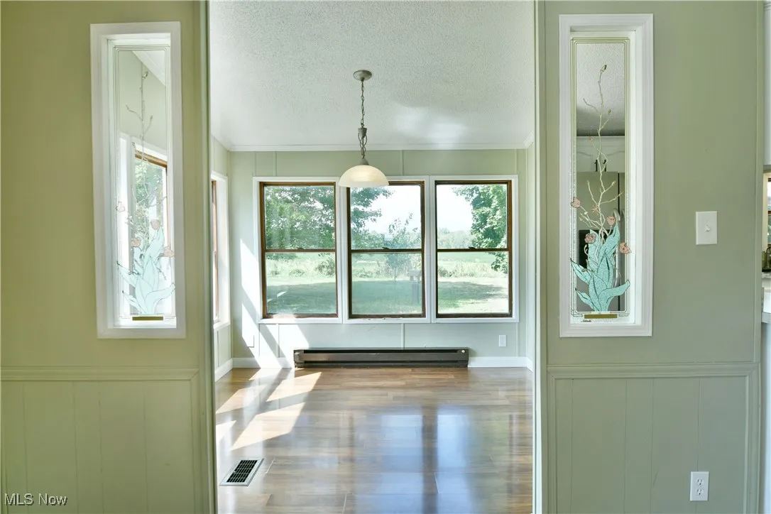 Doorway featuring a textured ceiling, plenty of natural light, a wainscoted wall, a baseboard heating unit, and crown molding