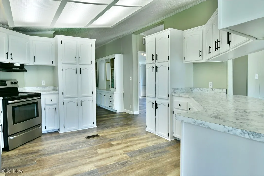 Kitchen with stainless steel range with electric stovetop, white cabinets, light countertops, light wood-style floors, and under cabinet range hood
