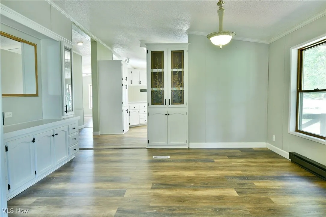 Unfurnished dining area featuring dark wood-style floors, a textured ceiling, and ornamental molding