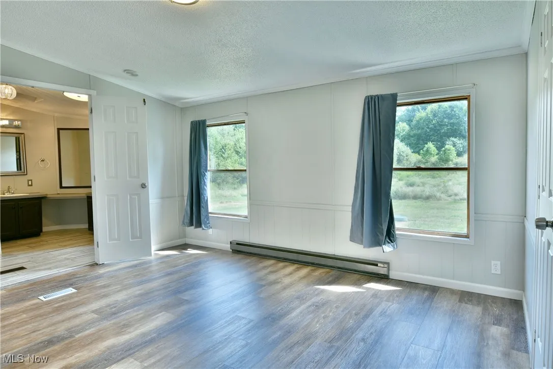 Empty room featuring a baseboard radiator, a textured ceiling, wood finished floors, and wainscoting