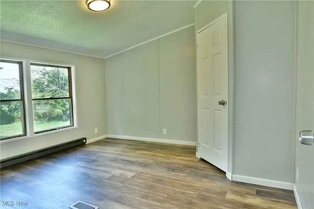 Empty room featuring baseboard heating, wood finished floors, a textured ceiling, and crown molding