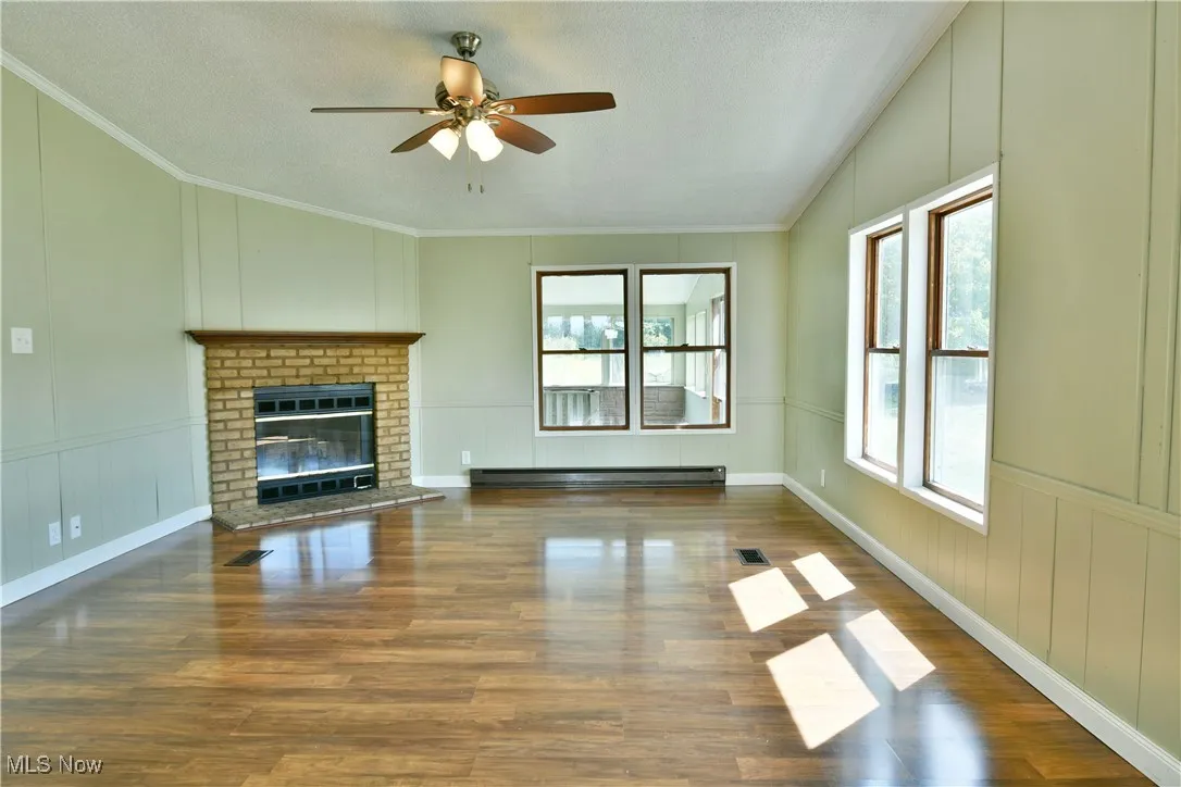 Unfurnished living room featuring a decorative wall, a brick fireplace, healthy amount of natural light, wood finished floors, and ornamental molding