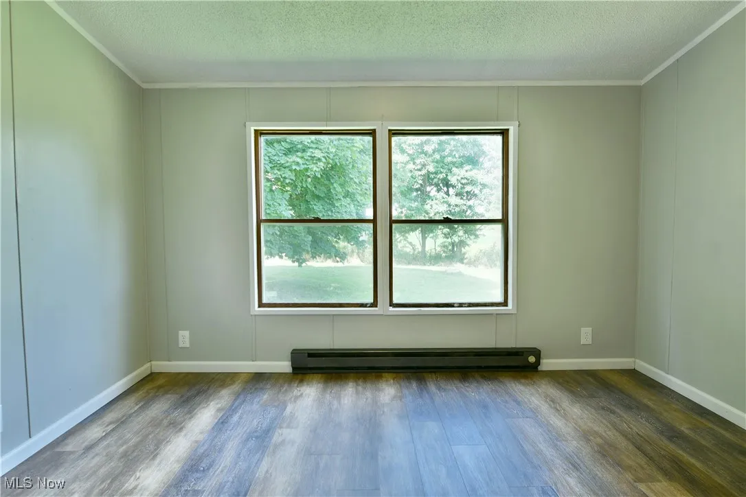 Empty room featuring a baseboard radiator, dark wood finished floors, a textured ceiling, and ornamental molding
