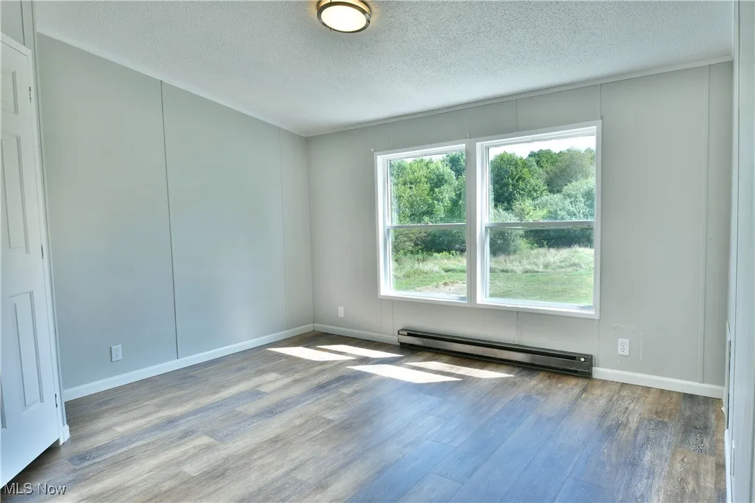 Empty room with baseboard heating, wood finished floors, and a textured ceiling