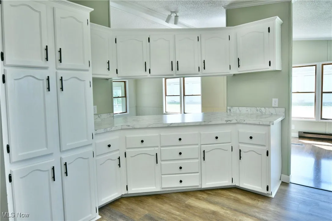 Kitchen with a textured ceiling, white cabinets, light countertops, light wood finished floors, and healthy amount of natural light