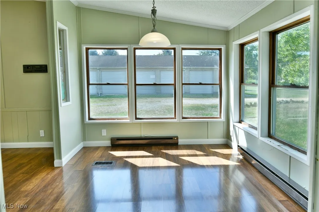 Unfurnished dining area with a baseboard heating unit, dark wood finished floors, a textured ceiling, ornamental molding, and vaulted ceiling
