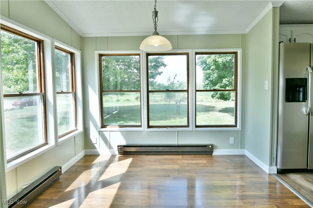 Unfurnished dining area featuring baseboard heating, wood finished floors, ornamental molding, and a textured ceiling
