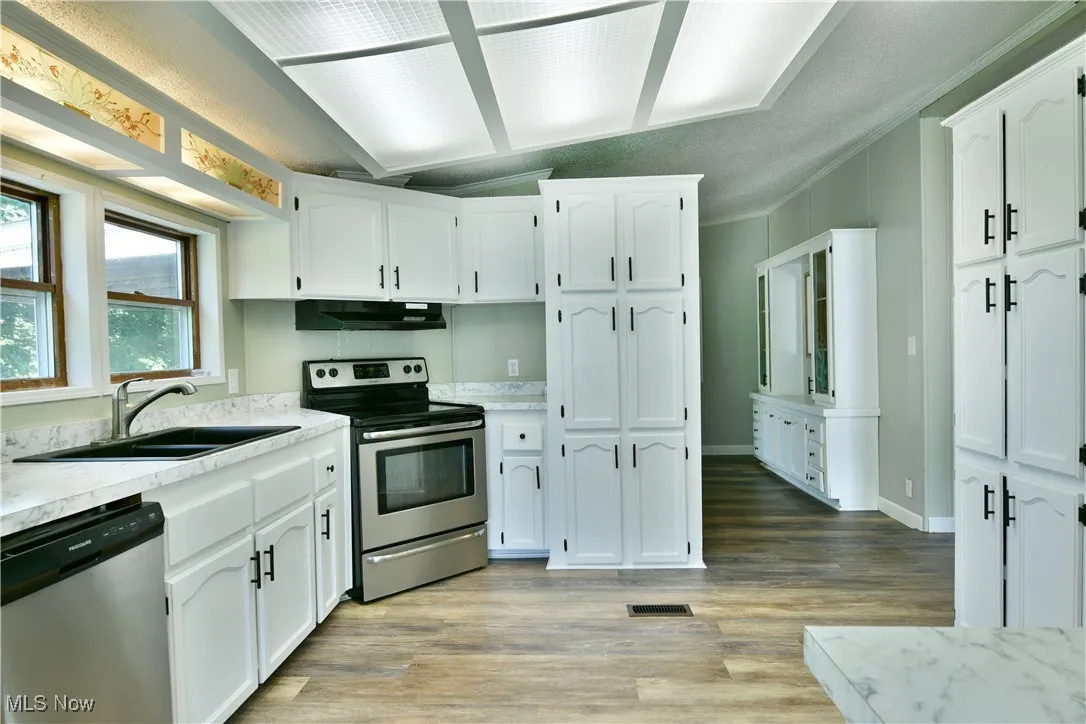 Kitchen featuring appliances with stainless steel finishes, light countertops, white cabinets, light wood-type flooring, and under cabinet range hood