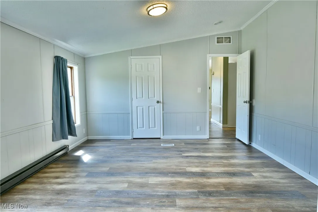 Unfurnished bedroom with a baseboard heating unit, crown molding, wood finished floors, a textured ceiling, and vaulted ceiling