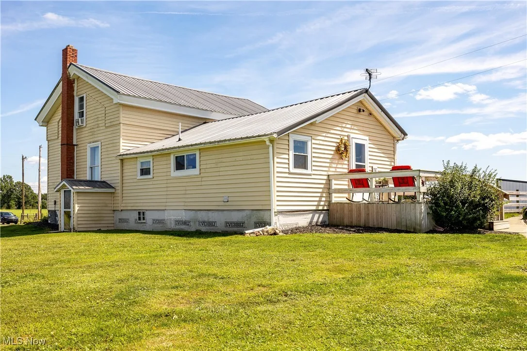 Rear view of house featuring a metal roof, a chimney, crawl space, and a lawn