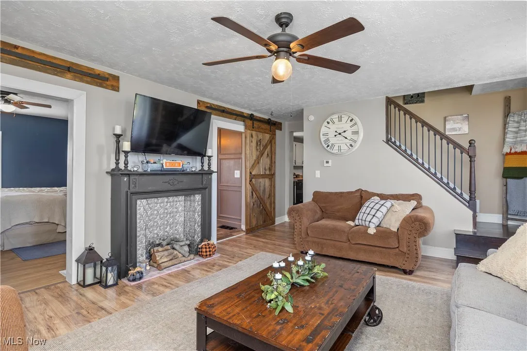 Living area featuring ceiling fan, a barn door, wood finished floors, a textured ceiling, and a fireplace