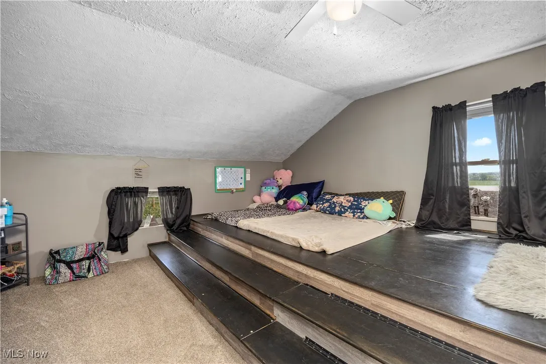 Carpeted bedroom featuring a textured ceiling, vaulted ceiling, and a ceiling fan