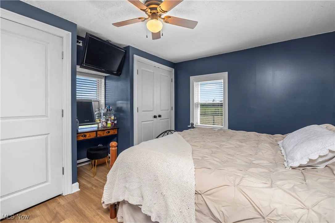 Bedroom with light wood finished floors, a textured ceiling, a ceiling fan, and two closets