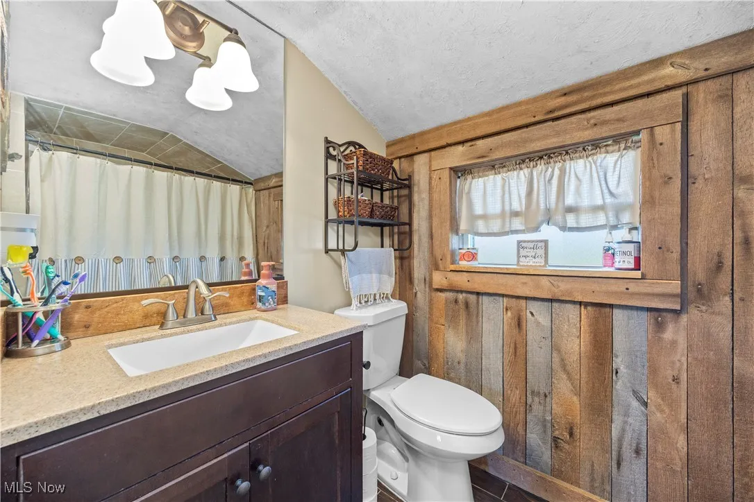 Bathroom featuring vanity, vaulted ceiling, a textured ceiling, a shower with curtain, and wooden walls