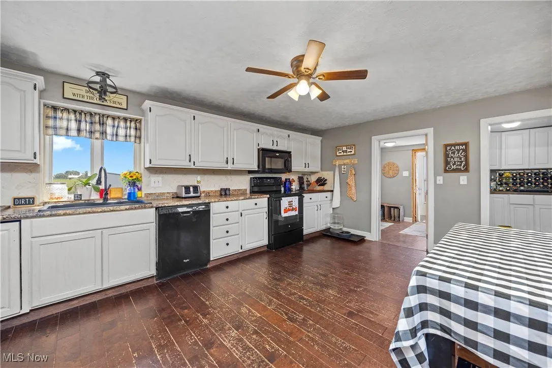 Kitchen with white cabinets, black appliances, backsplash, dark wood-type flooring, and ceiling fan