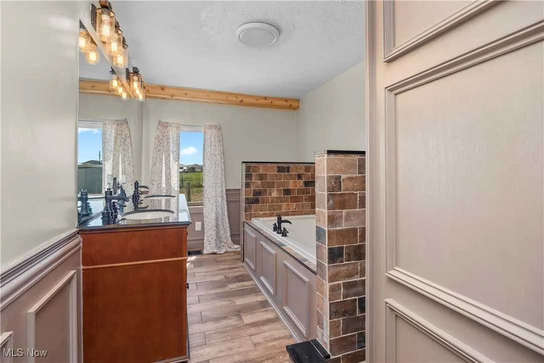 Full bathroom featuring wainscoting, a bath, vanity, light wood-style flooring, and a textured ceiling