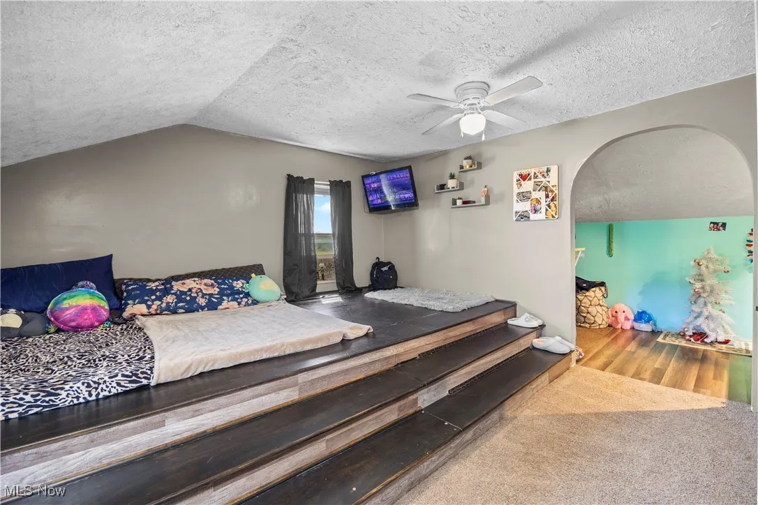 Bedroom featuring a textured ceiling, a ceiling fan, vaulted ceiling, wood finished floors, and arched walkways