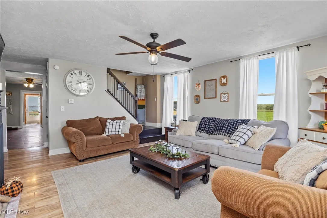 Living room featuring a ceiling fan, light wood-style flooring, a textured ceiling, and stairs