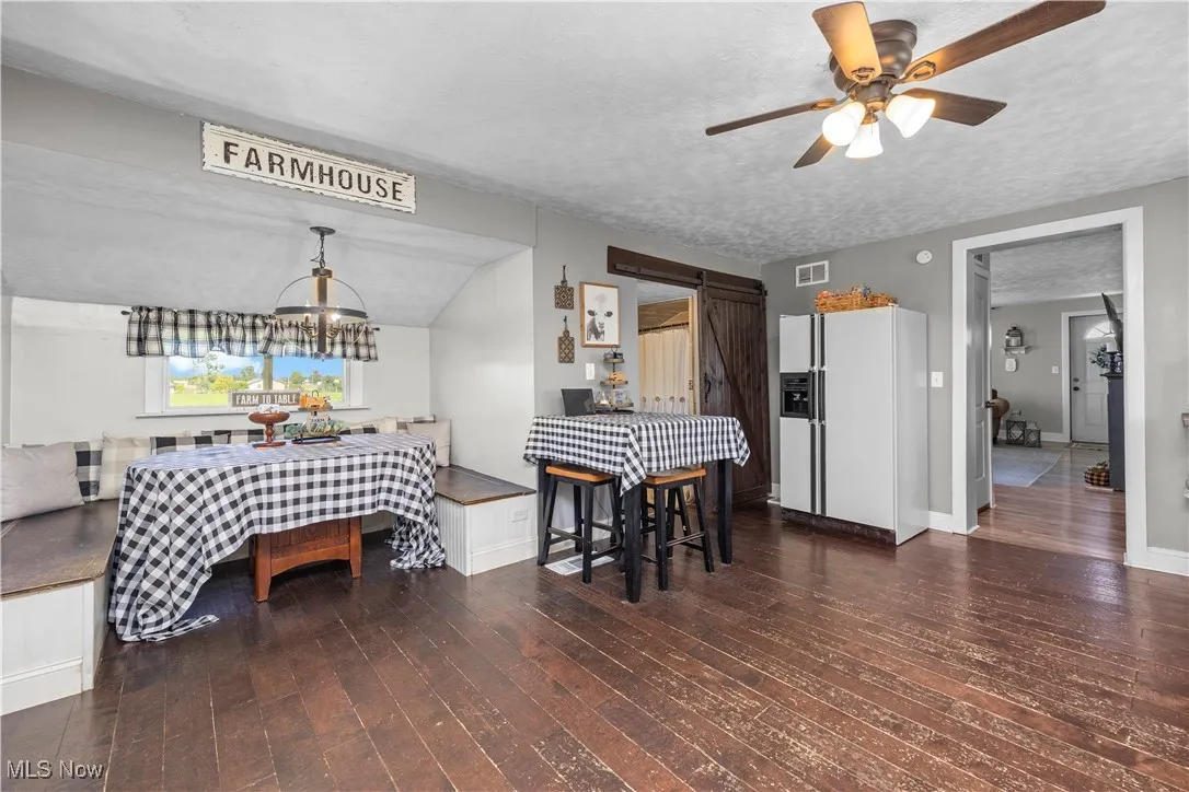 Dining area with a barn door, dark wood-type flooring, vaulted ceiling, a textured ceiling, and ceiling fan