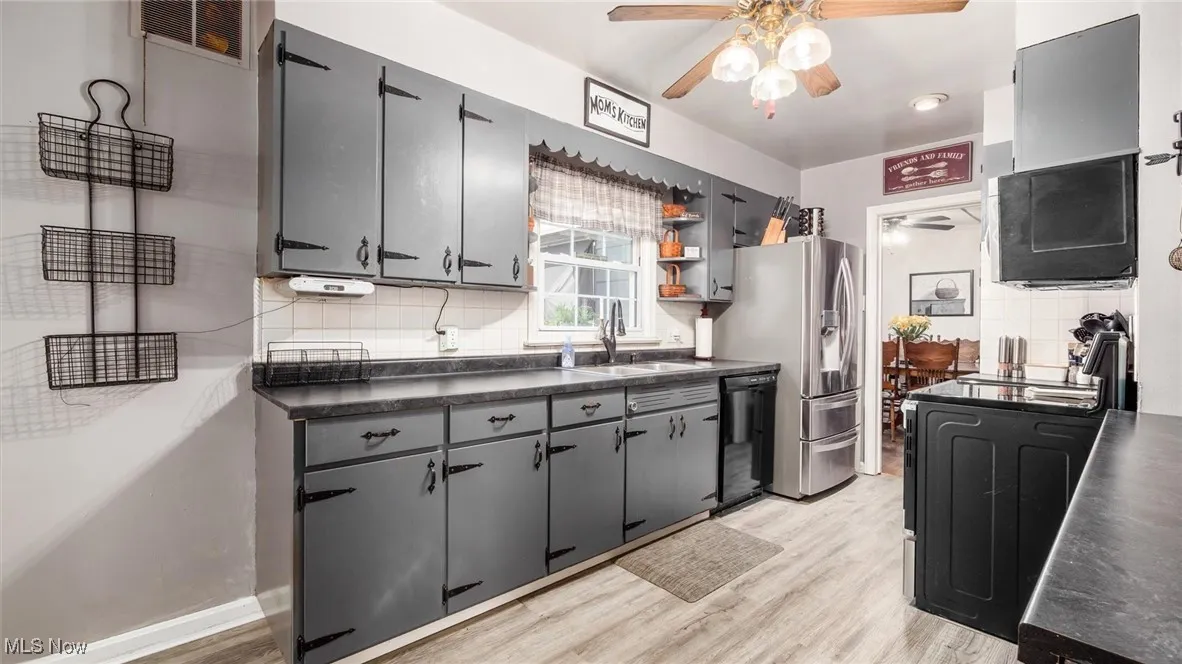Kitchen with dark countertops, backsplash, gray cabinetry, ceiling fan, and light wood-style floors