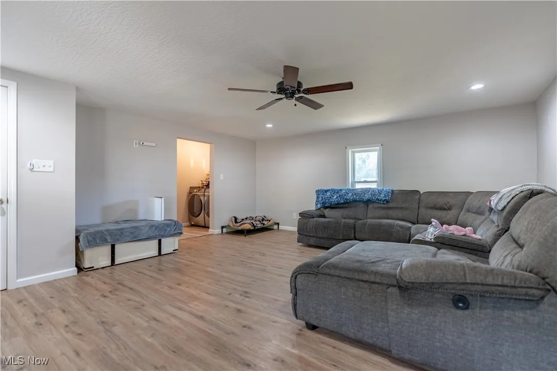 Living room with light wood finished floors, washer and clothes dryer, a ceiling fan, and recessed lighting