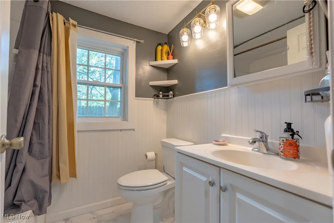 Full bathroom with a wainscoted wall, vanity, and light marble finish floors