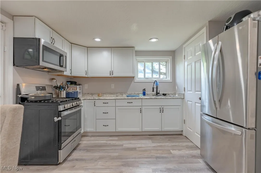 Kitchen featuring appliances with stainless steel finishes, white cabinets, light wood-type flooring, light stone countertops, and recessed lighting