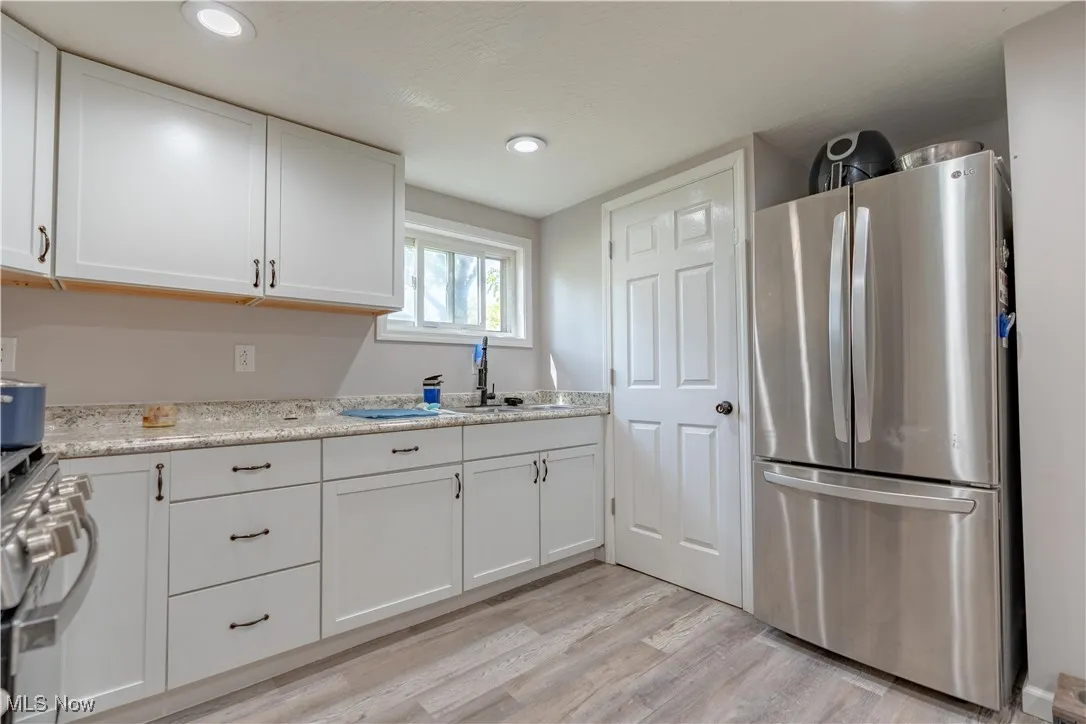 Kitchen with appliances with stainless steel finishes, white cabinetry, light wood-style flooring, recessed lighting, and light stone countertops
