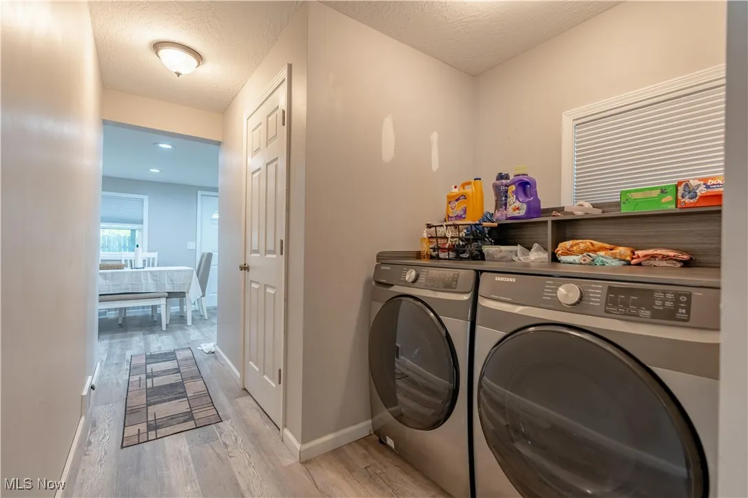 Washroom with light wood-style flooring, washing machine and clothes dryer, and a textured ceiling