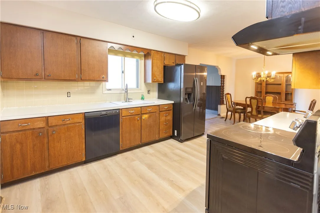 Kitchen featuring black appliances, island range hood, backsplash, light wood-style flooring, and a chandelier