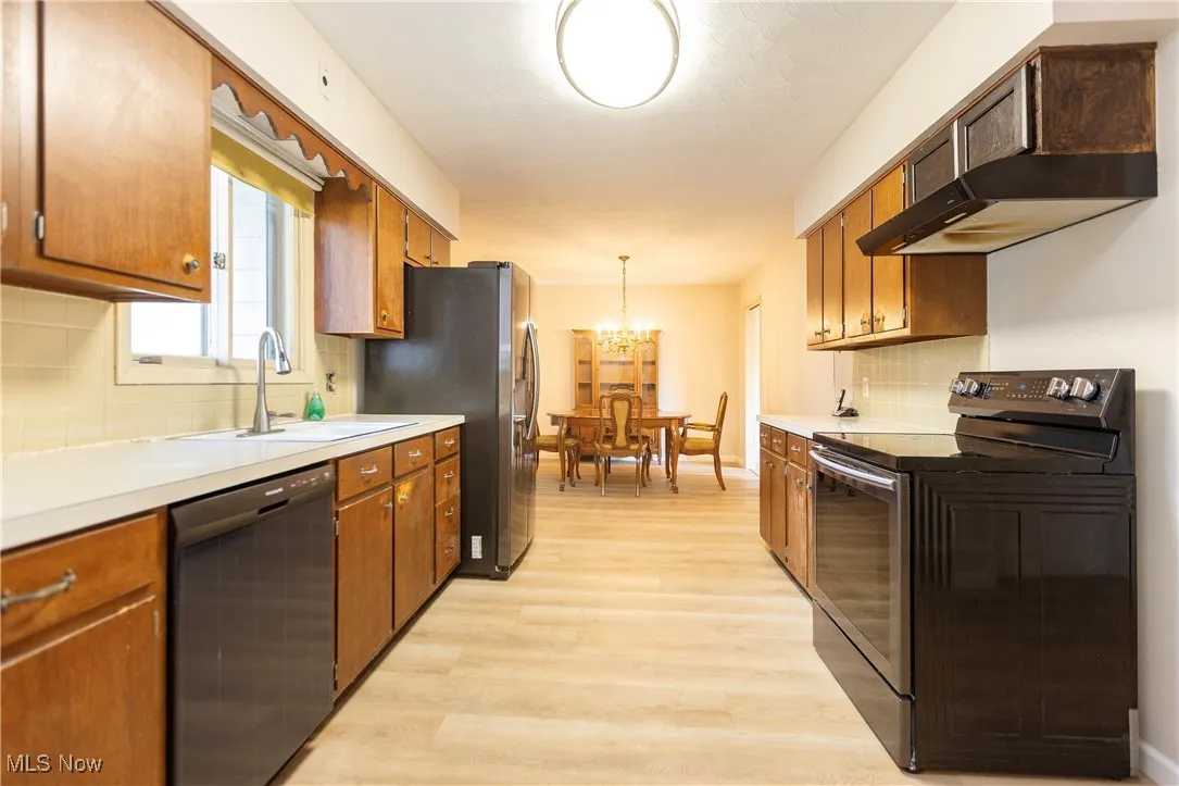 Kitchen featuring decorative backsplash, black range with electric stovetop, a chandelier, dishwasher, and light countertops