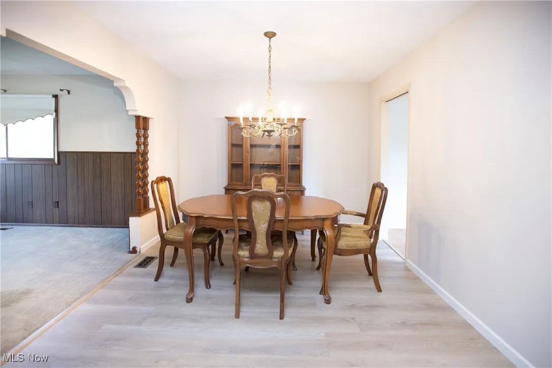 Dining space featuring wooden walls, a chandelier, light wood finished floors, and wainscoting
