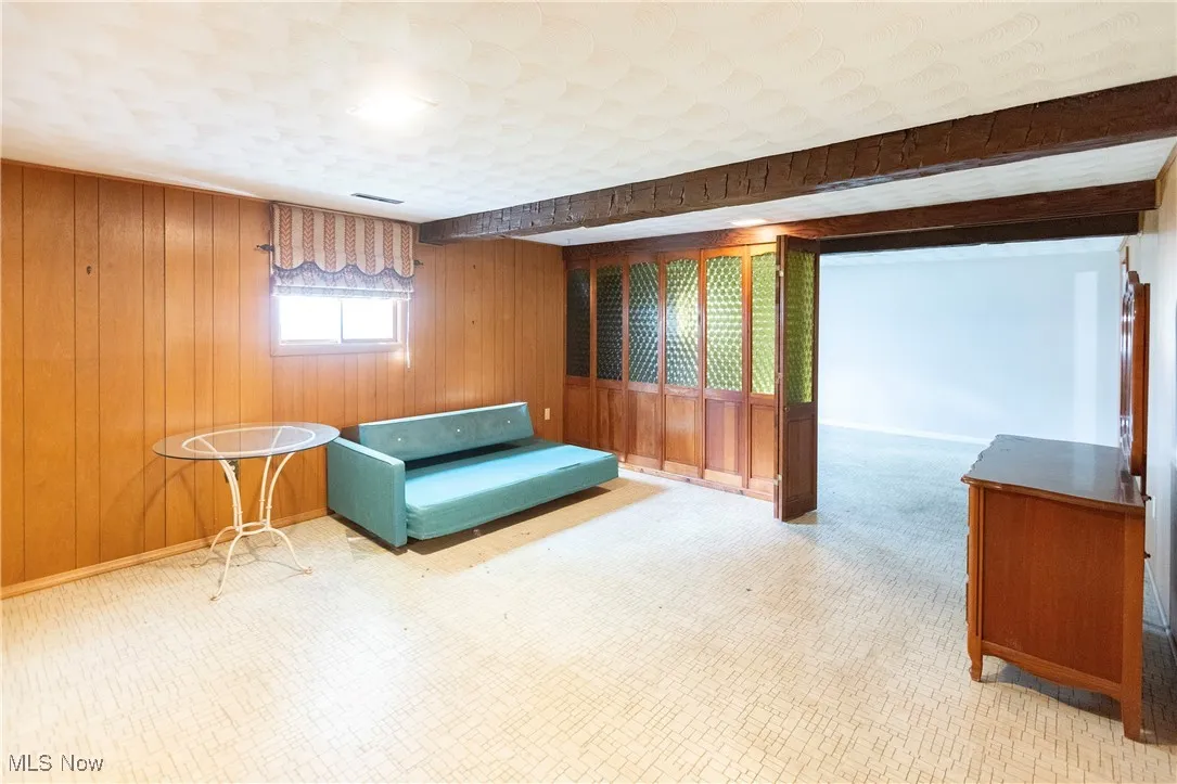 Living area with wood walls, tile patterned floors, and beamed ceiling
